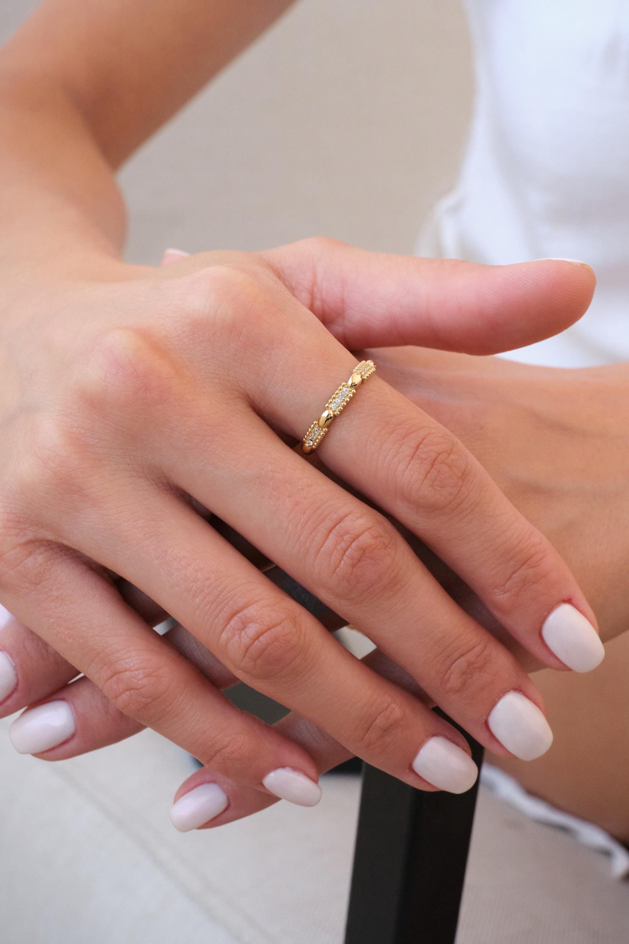 May include: A gold ring with a repeating heart and diamond design. The ring is worn on a finger, and the hand is in focus. The ring is made of gold and has small diamonds set into the design. The ring is a piece of jewelry.