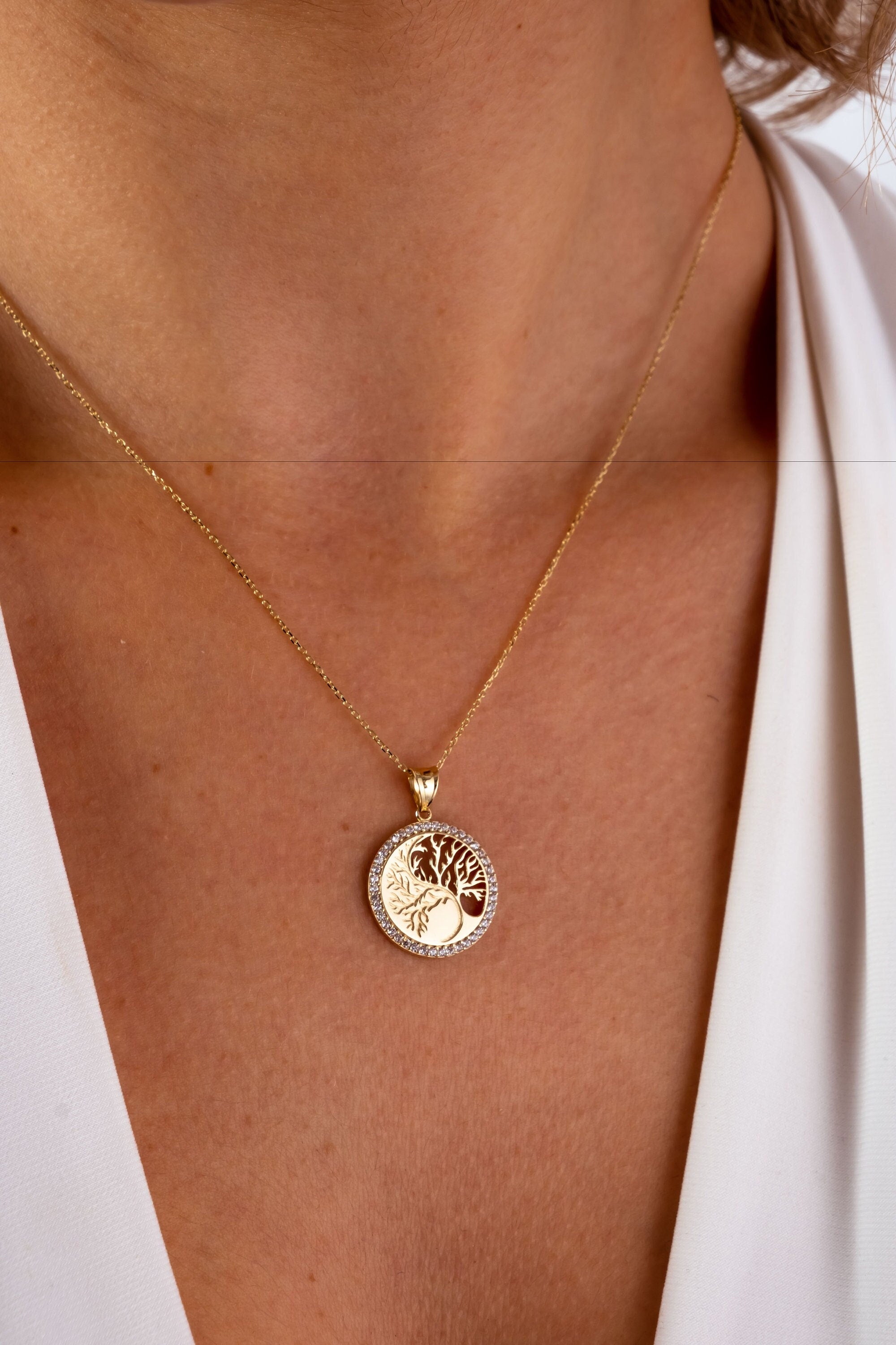 May include: A gold necklace with a round pendant featuring a tree of life design with clear cubic zirconia stones.