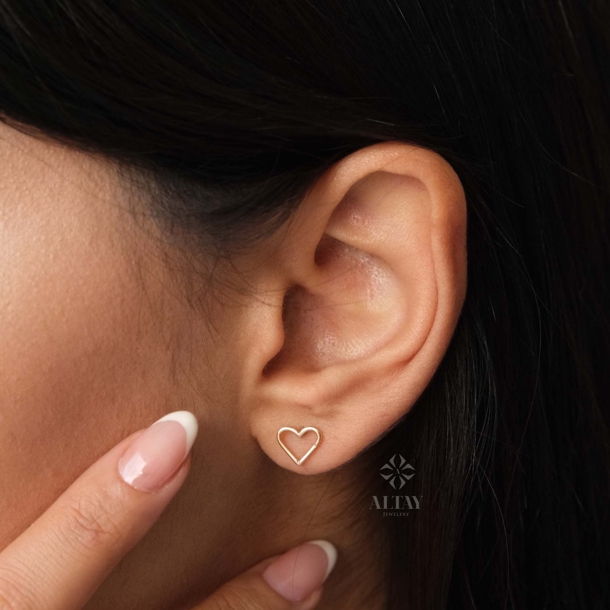 May include: A pair of gold heart-shaped earrings. The earrings are small and delicate, and they are worn in the wearer's earlobes.