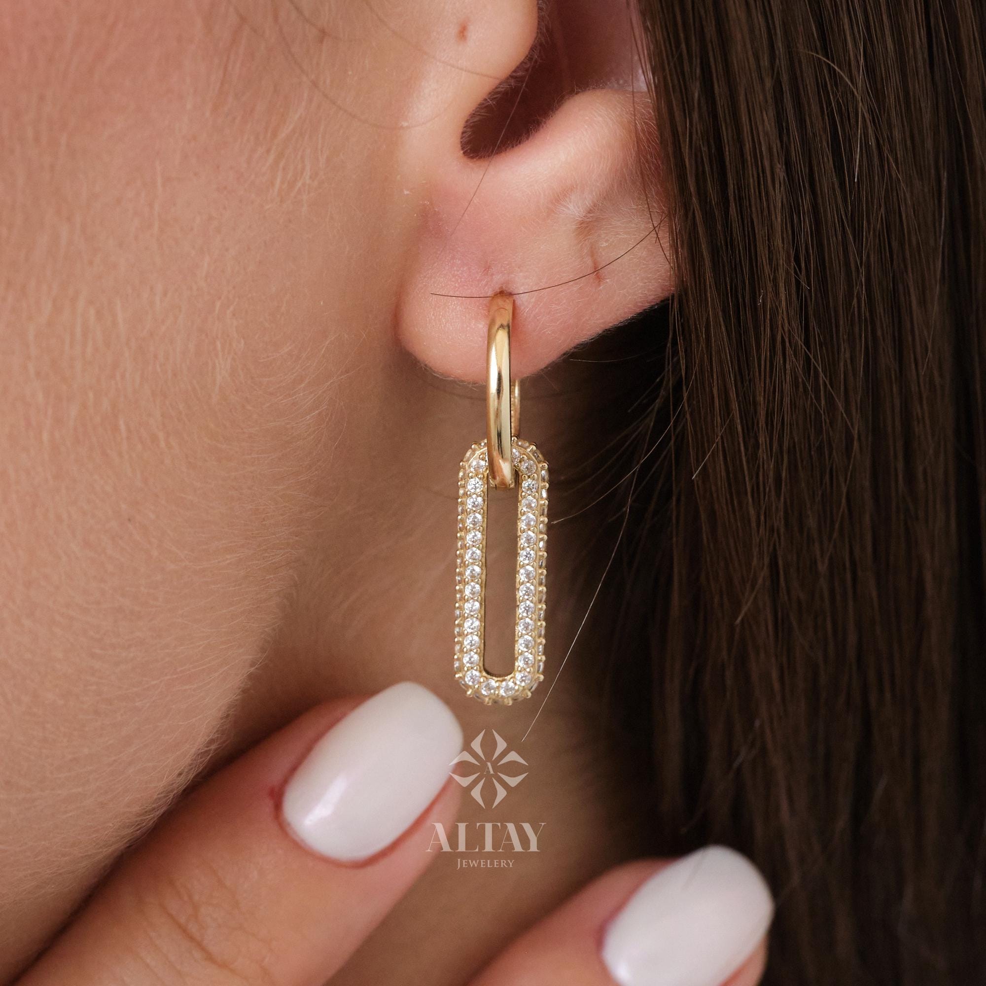 May include: Gold hoop earrings with a rectangular, diamond-studded pendant. The earrings are worn on a person's ear. The brand name "ALTAY JEWELRY" is visible in the lower right corner of the image.