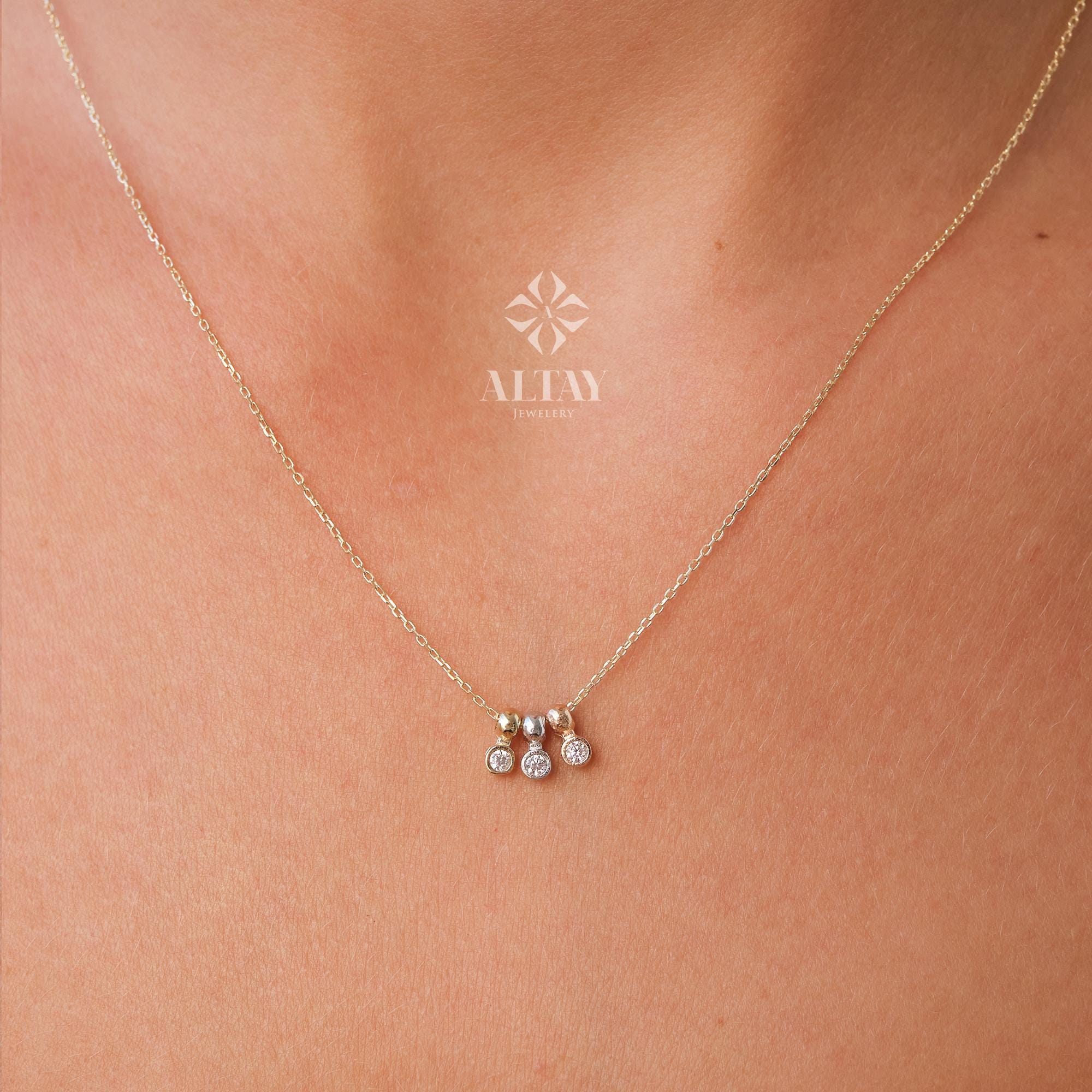 May include: A delicate gold necklace with three small, sparkling diamond pendants. The necklace is displayed against a skin tone background. The brand name "ALTAY Jewelry" is visible in the upper center.