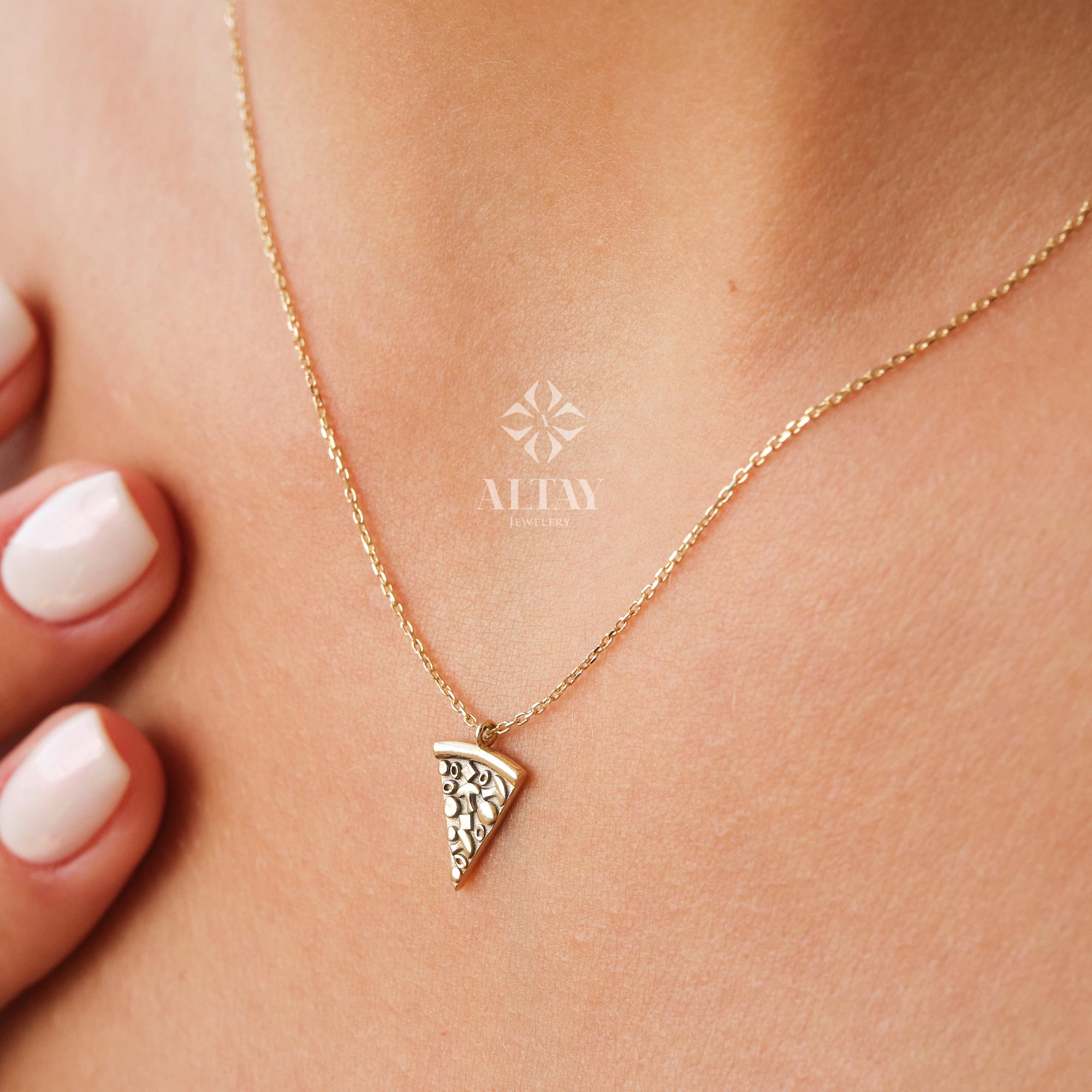 May include: A gold-colored necklace with a pizza slice pendant. The pendant has a detailed design and is suspended from a delicate chain. The necklace is worn on a person's neck.