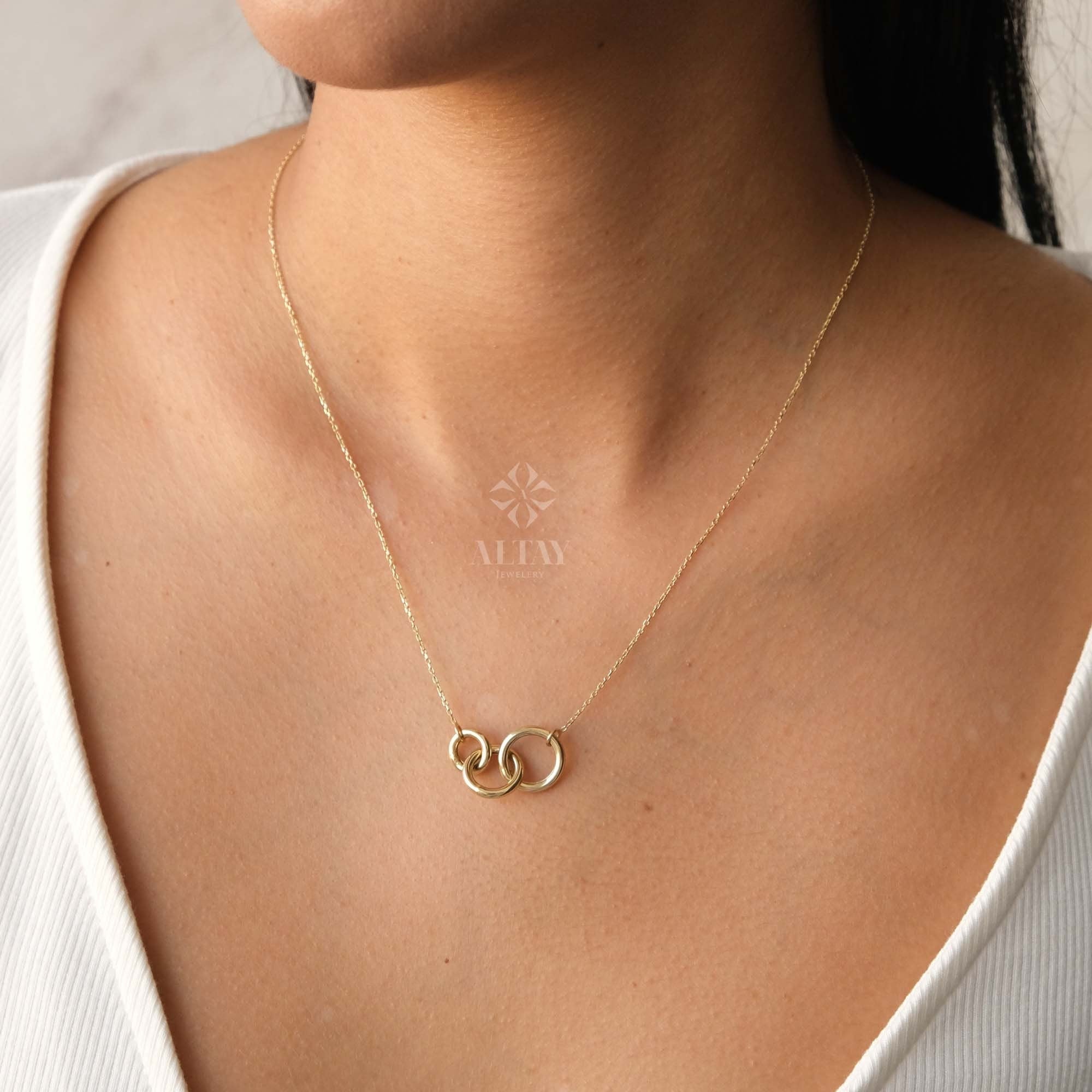 May include: A gold necklace with three interlocking circles. The necklace is on a model wearing a white shirt.