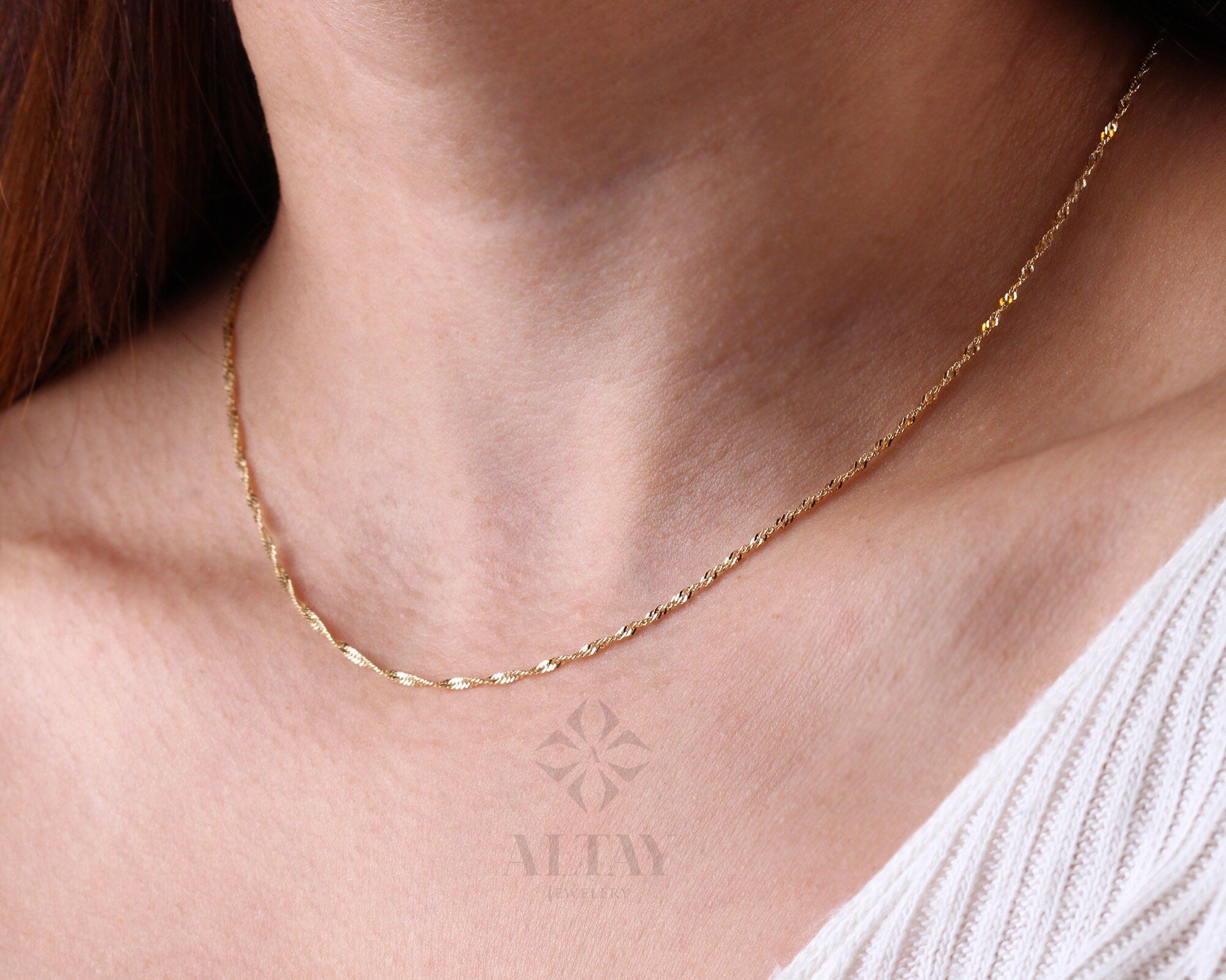 May include: A delicate gold chain necklace with a twisted design. The chain is thin and has a subtle shine.