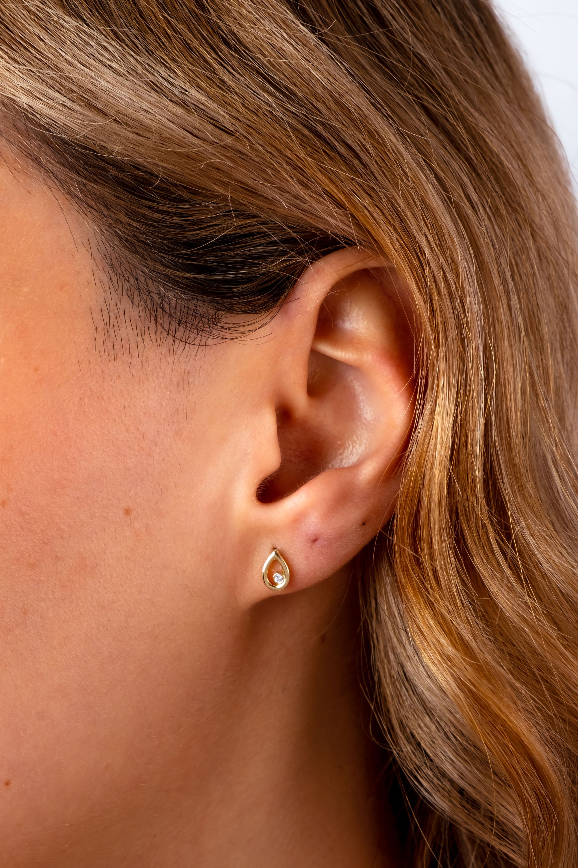 May include: A gold teardrop-shaped earring with a small clear stone in the center.