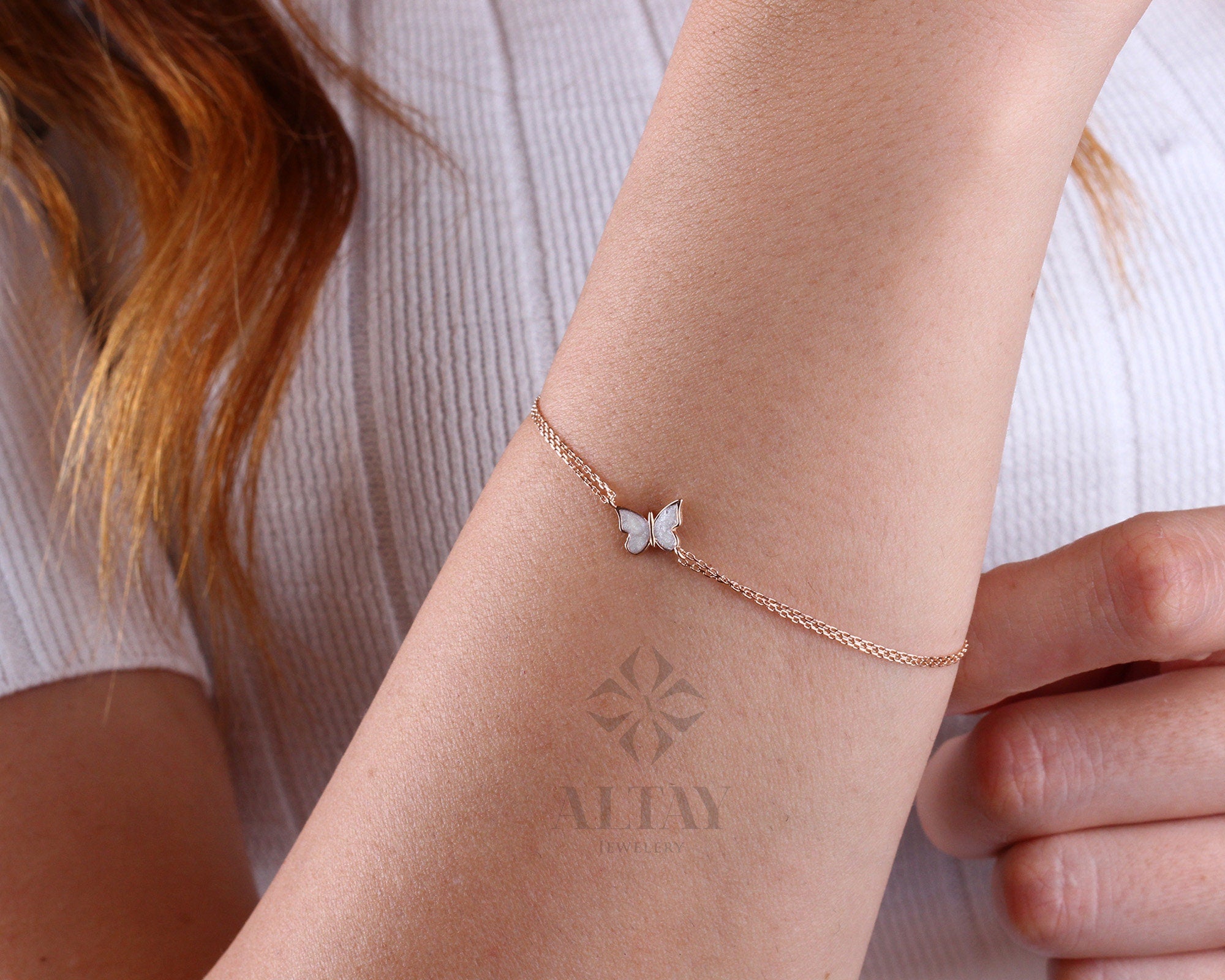 May include: A delicate gold chain bracelet with a white butterfly charm. The butterfly has a detailed design and is set with small sparkling stones.