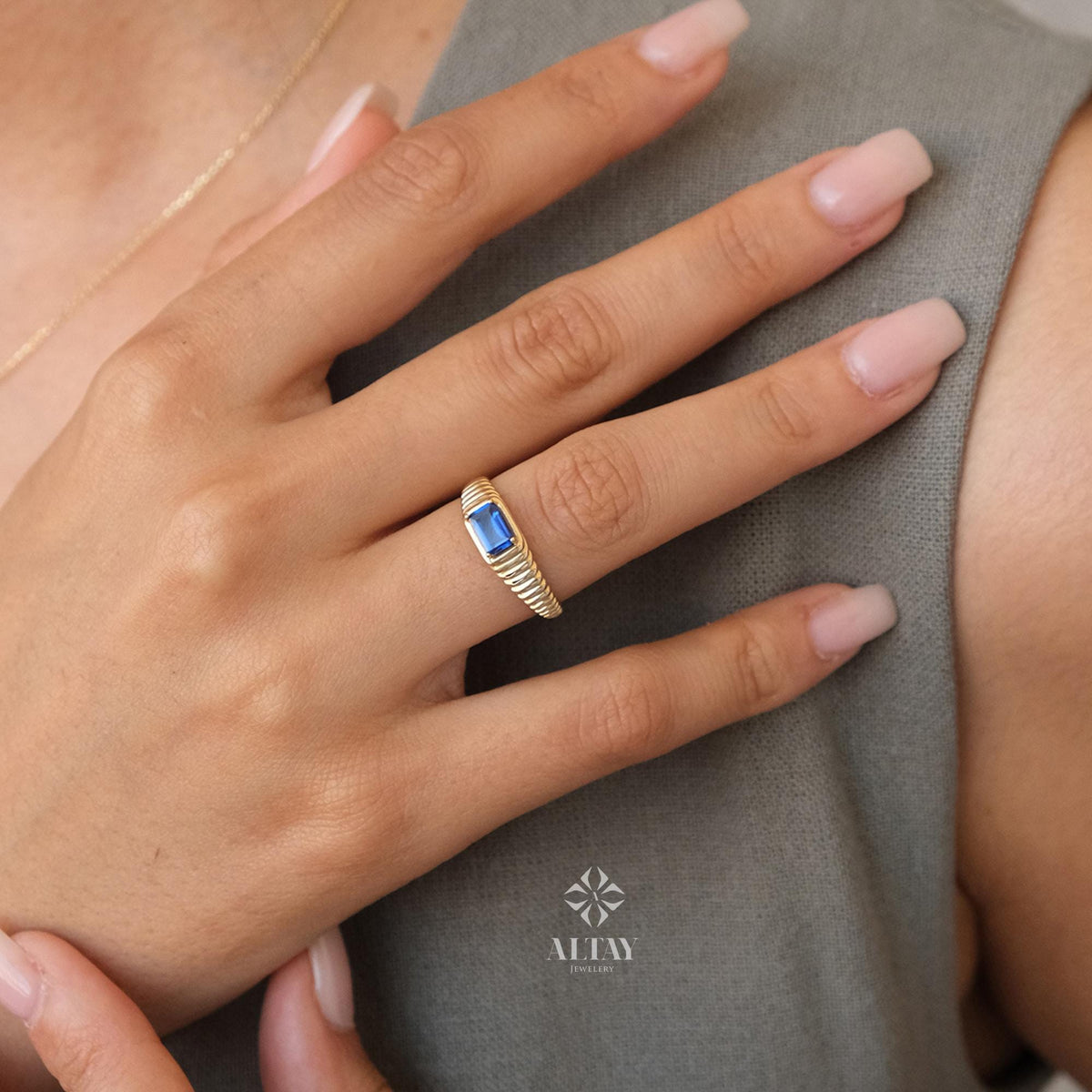 May include: A gold ring with a blue gemstone set in a rectangular shape. The ring has a textured band.